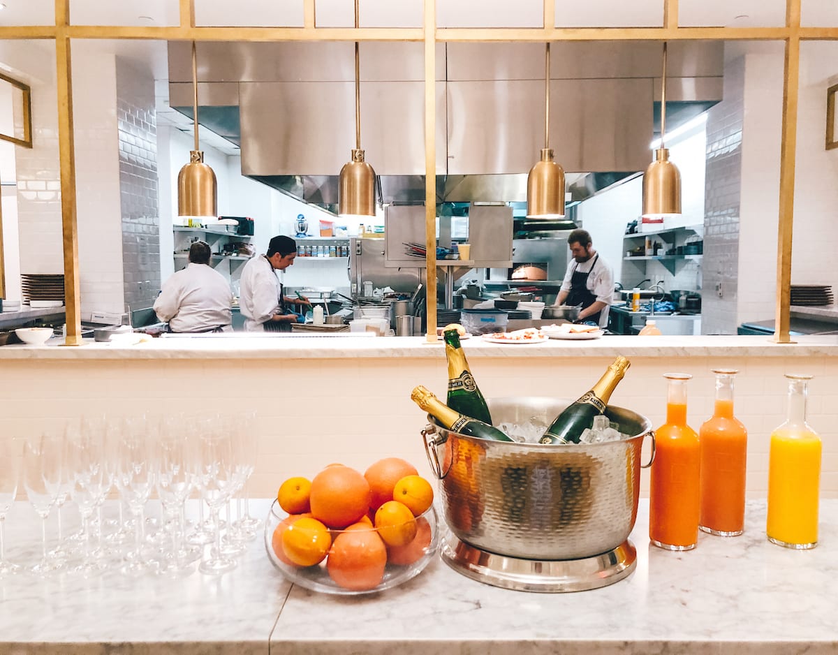 champagne on ice, oranges on bowl, juice bottles and open kitchen window